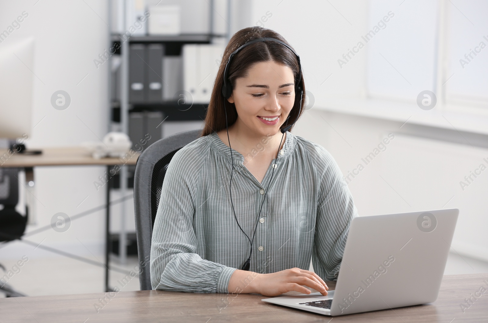 Photo of Hotline operator with headset working on laptop in office