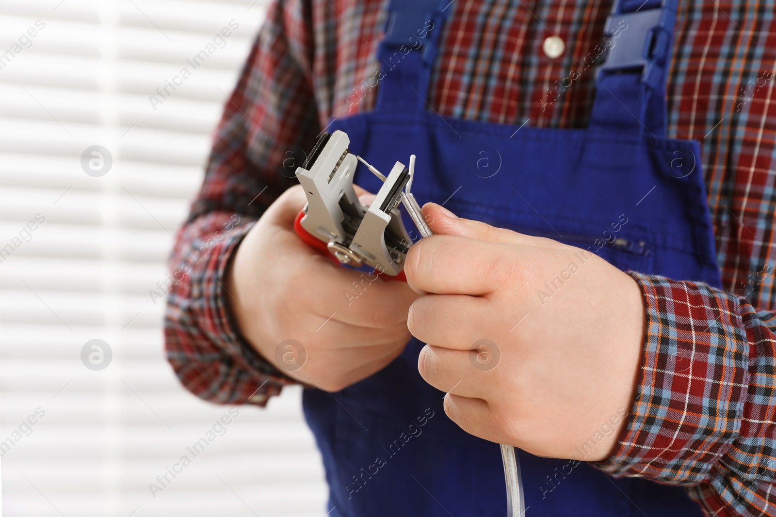 Photo of Professional electrician in uniform stripping wiring indoors, closeup