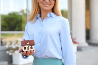 Photo of Female real estate agent with house model outdoors