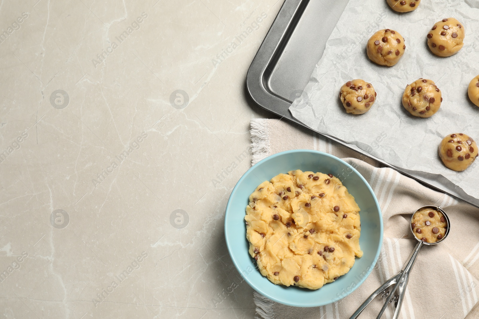 Photo of Bowl with dough and uncooked chocolate chip cookies on light grey table, flat lay. Space for text