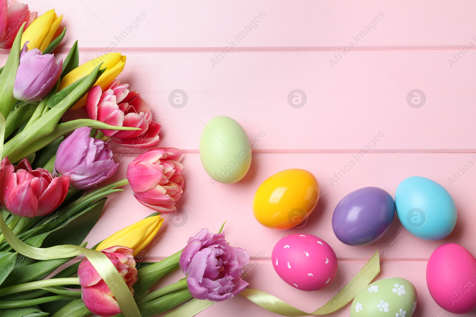 Photo of Bright painted eggs and spring tulips on pink wooden table, flat lay with space for text. Happy Easter