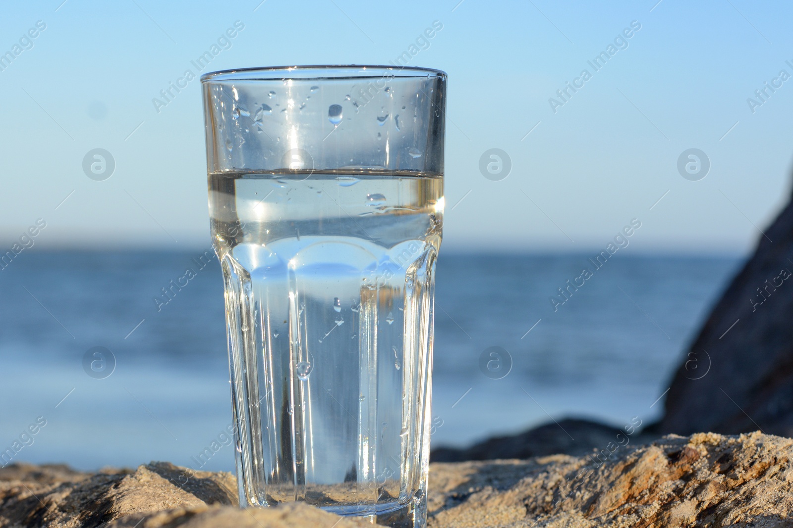 Photo of Glass of clean water on rock near sea. Space for text