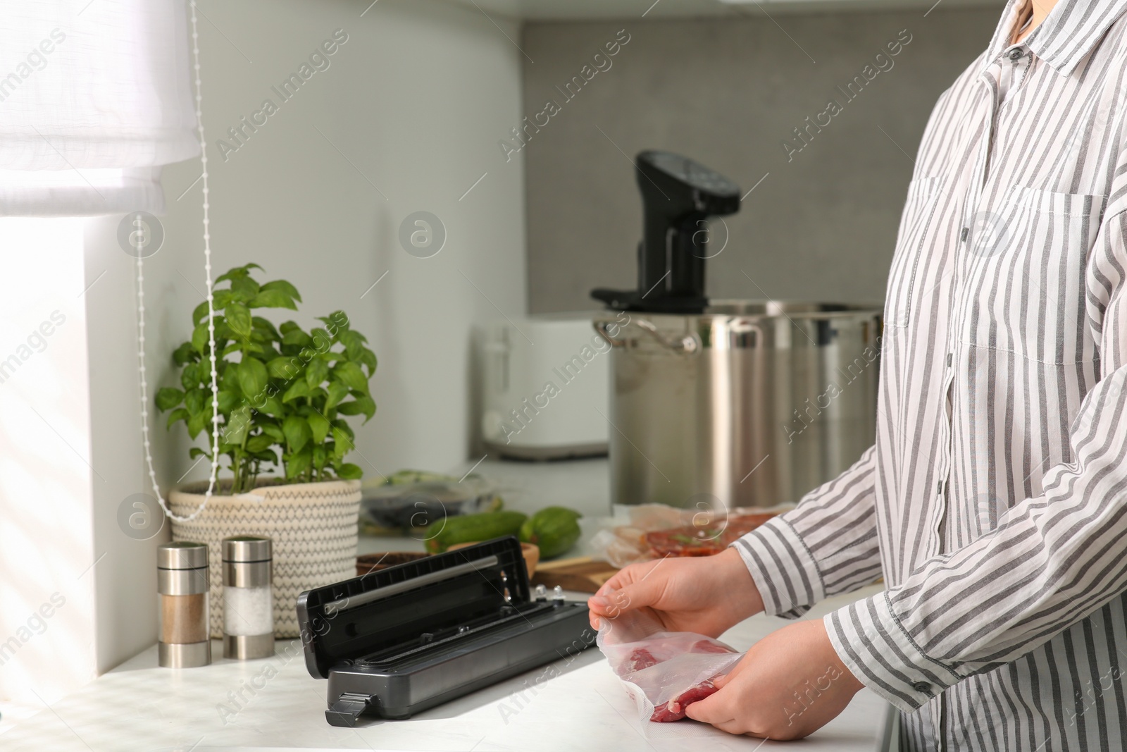 Photo of Woman using sealer for vacuum packing in kitchen, closeup. Sous vide cooking