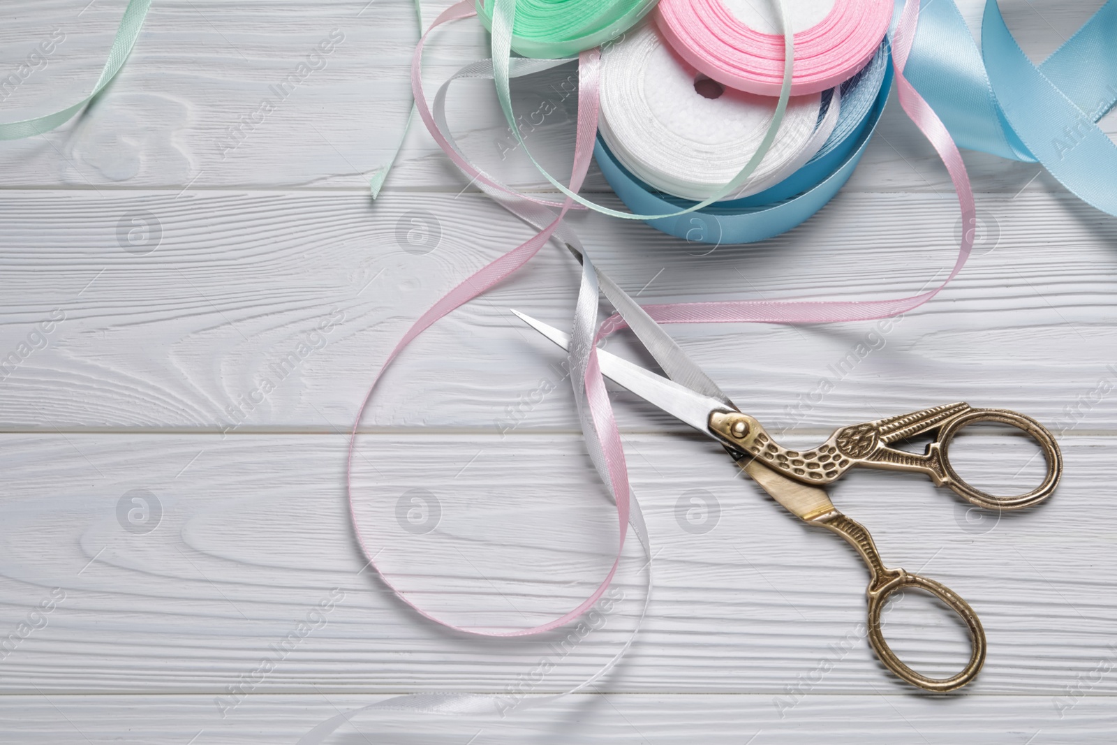 Photo of Pair of scissors with colorful ribbons on white wooden table, flat lay. Space for text