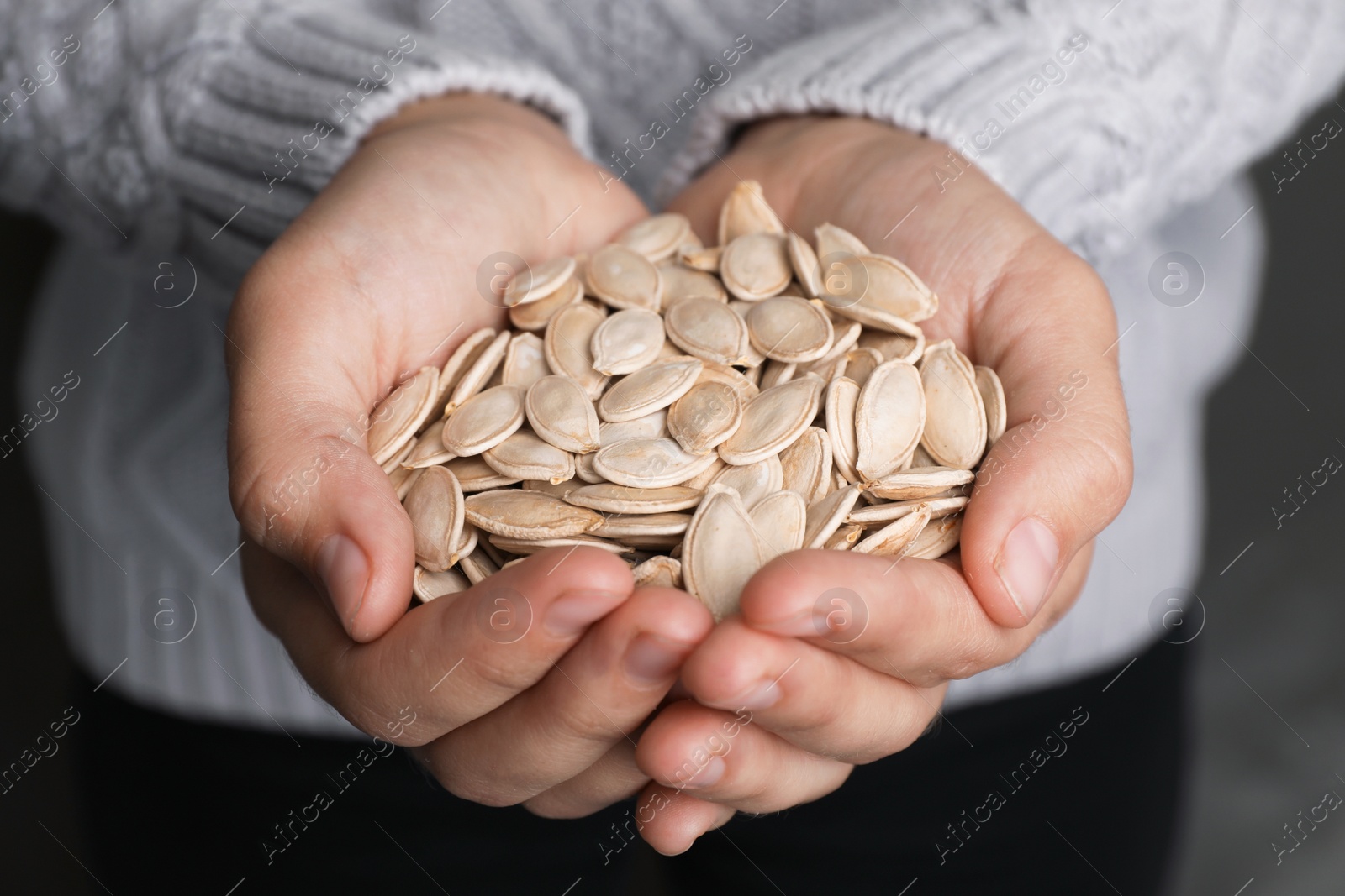 Photo of Woman holding raw pumpkin seeds, closeup view