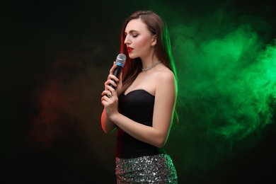 Photo of Beautiful woman with microphone singing in color lights on dark background