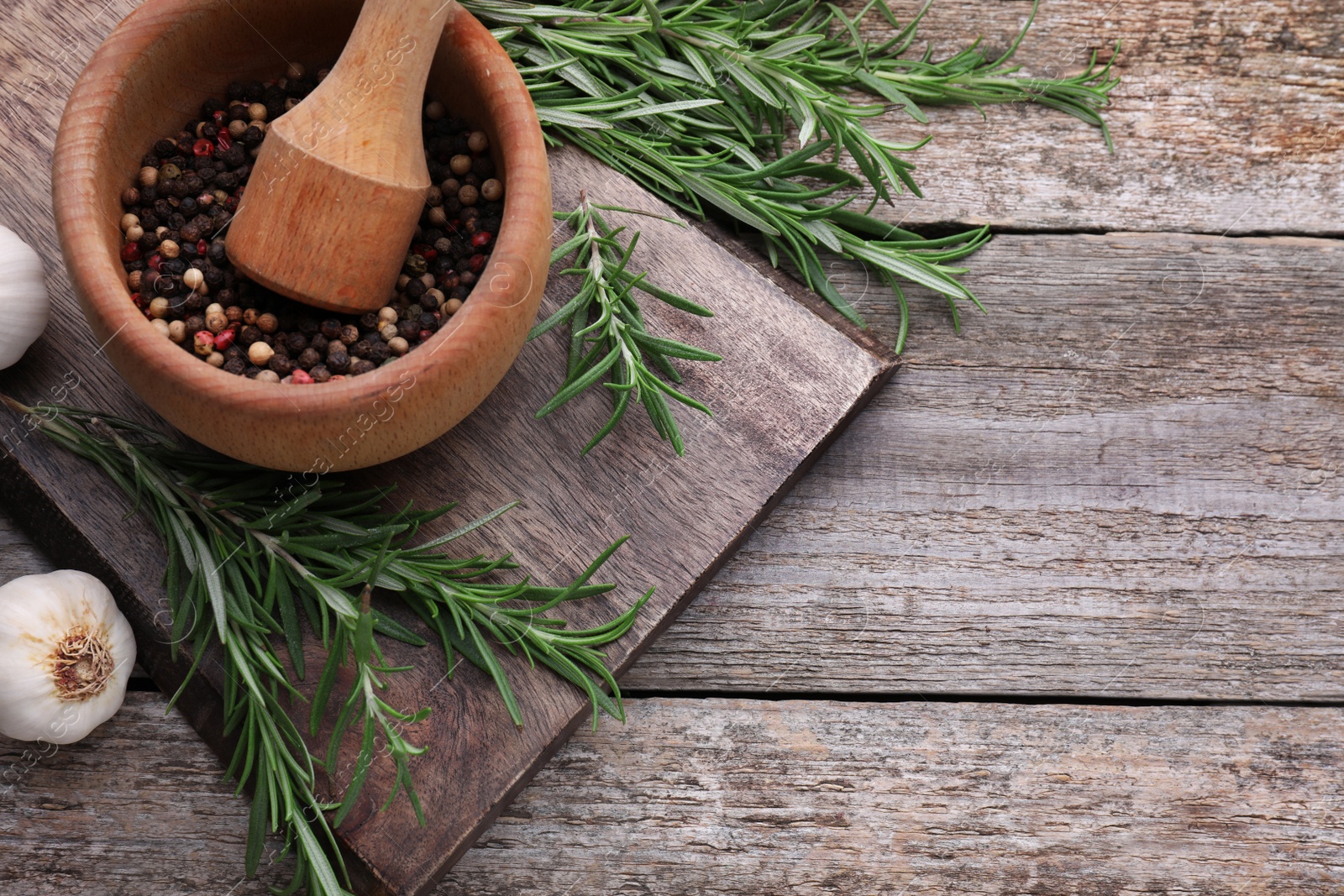 Photo of Fresh rosemary, mortar and garlic on wooden table, flat lay