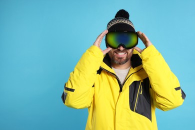 Winter sports. Happy man in ski suit and goggles on light blue background, space for text