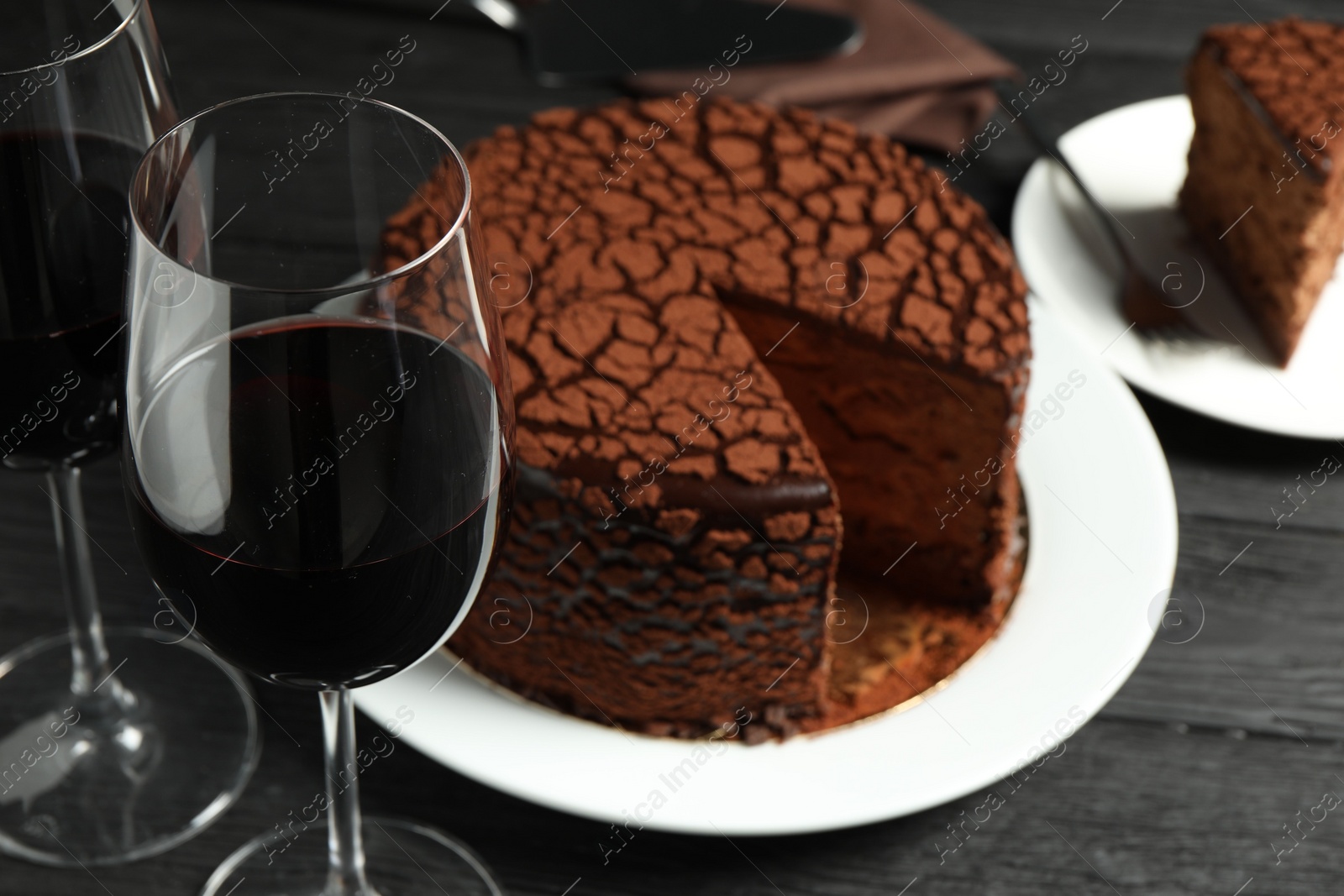 Photo of Delicious chocolate truffle cake and red wine on black wooden table