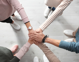 Photo of People holding hands together over light wooden background, top view. Unity concept