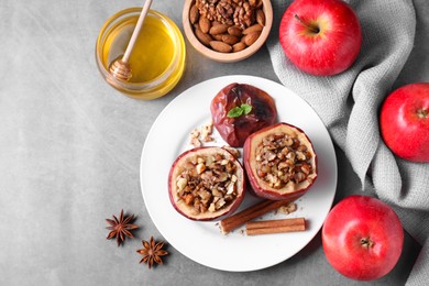 Tasty baked apples with nuts, honey and spices on gray table, flat lay. Space for text