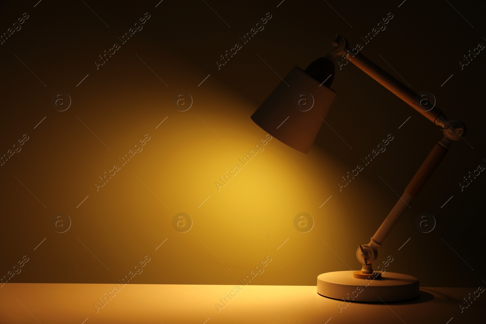 Photo of Stylish modern desk lamp on table at night, space for text