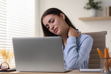 Young woman suffering from neck pain at table in office