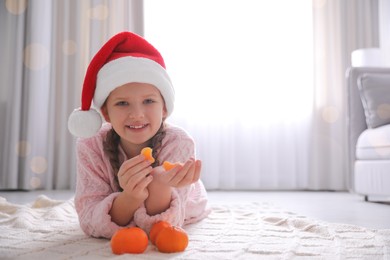 Photo of Happy girl in Santa hat with ripe tangerines on floor at home. Space for text