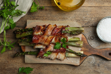 Photo of Oven baked asparagus wrapped with bacon on wooden table, flat lay