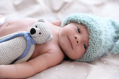 Photo of Cute newborn baby in warm hat with toy lying on bed