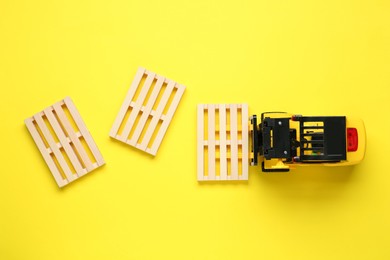 Photo of Toy forklift and wooden pallets on yellow background, flat lay