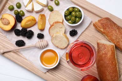 Photo of Glass of delicious rose wine and snacks on white wooden table, top view