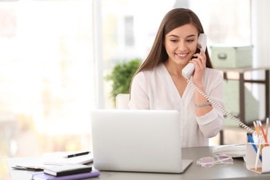 Photo of Young woman talking on phone at workplace