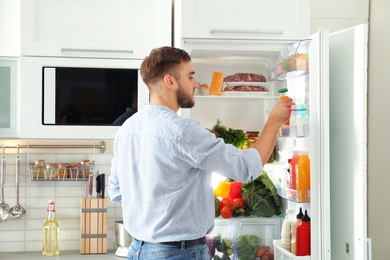 Man taking bottle with juice out of refrigerator in kitchen