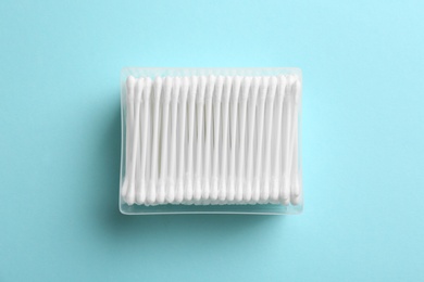 Plastic container with cotton swabs on color background, top view