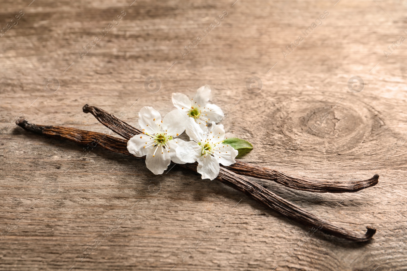 Photo of Vanilla sticks and flowers on wooden background