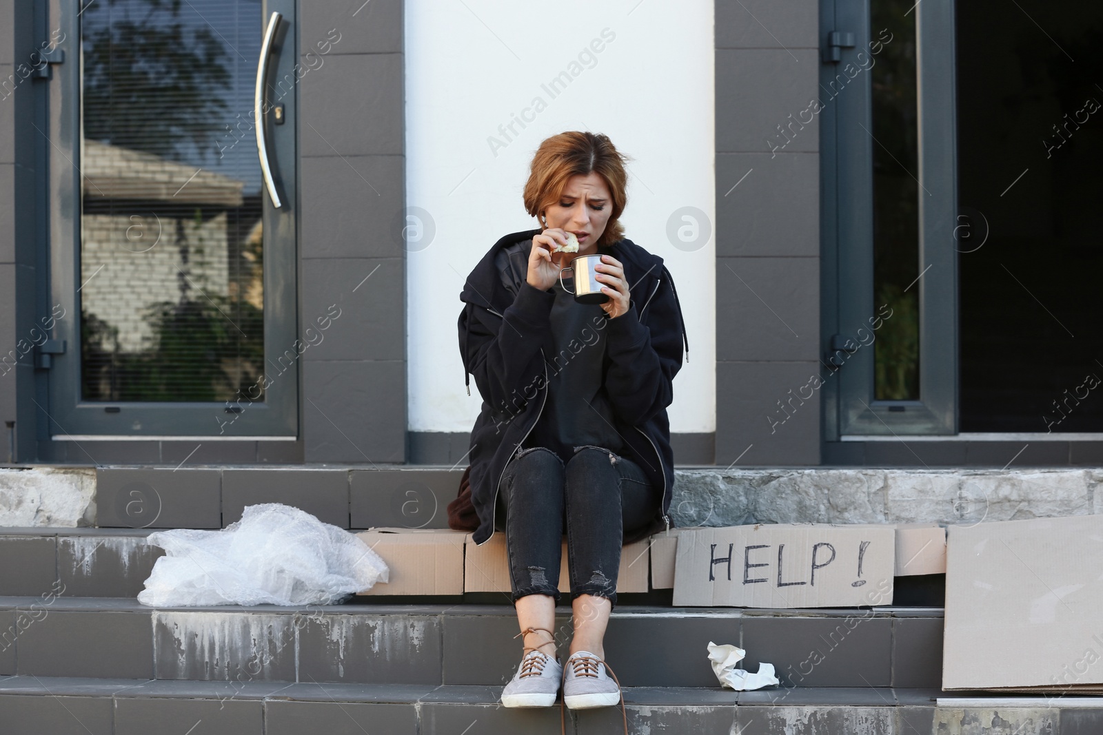 Photo of Poor woman with piece of bread and mug on city street