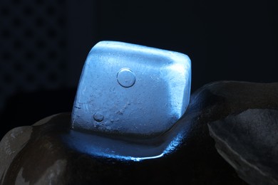 Photo of Crystal clear ice cube on stone against dark background, closeup. Color tone effect