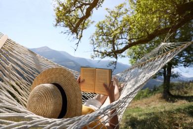 Photo of Young woman reading book in hammock outdoors on sunny day