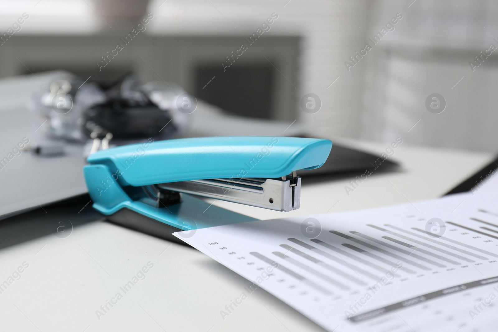 Photo of Stapler with document on white table indoors, closeup