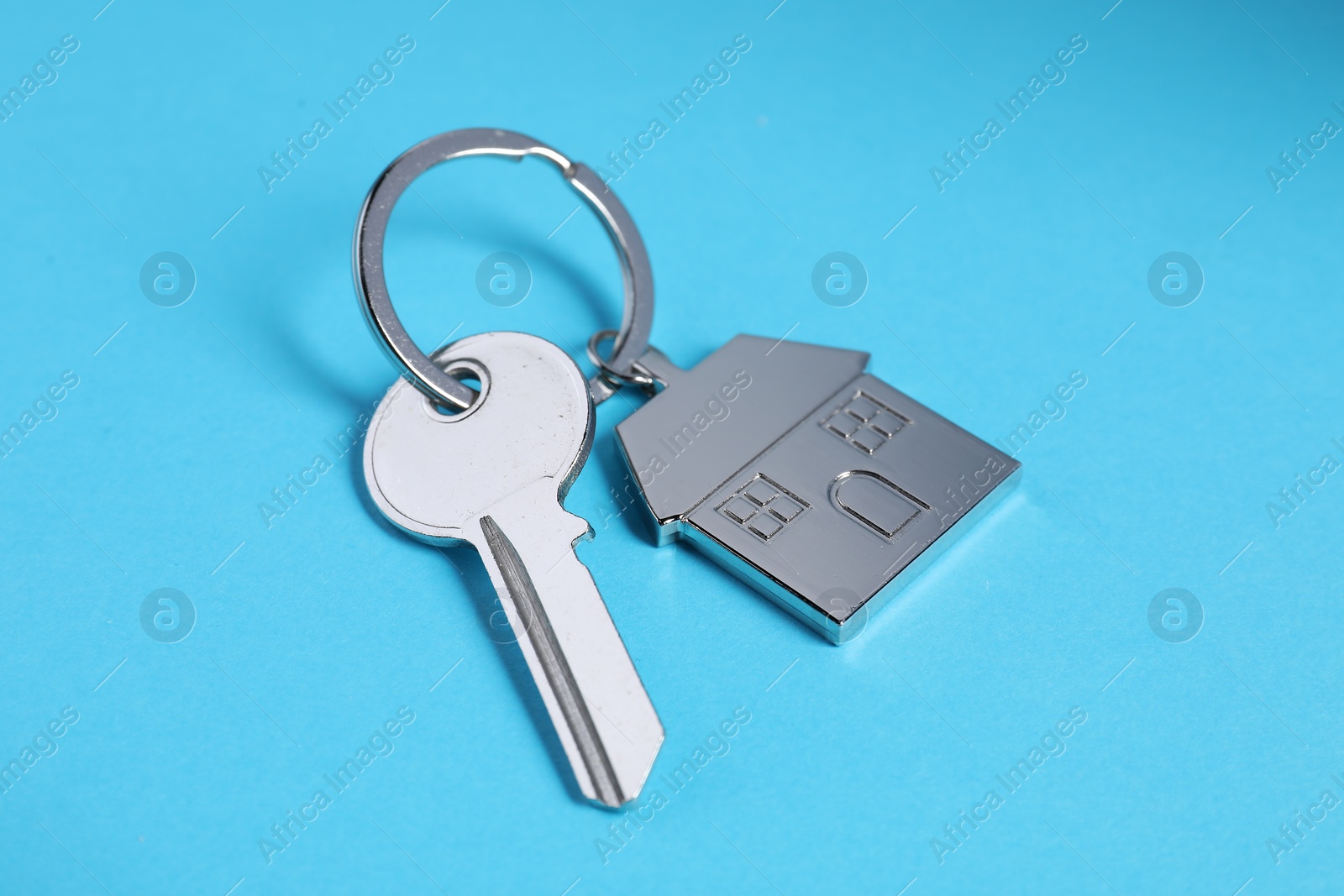 Photo of Key with keychain in shape of house on light blue background, closeup
