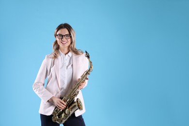 Beautiful young woman in elegant outfit with saxophone on light blue background. Space for text
