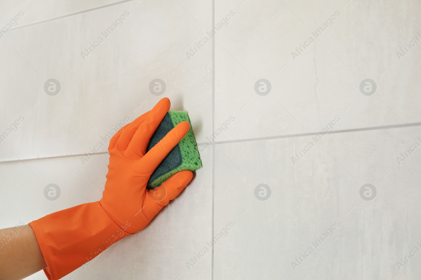 Photo of Woman in protective glove cleaning bathroom wall with sponge, closeup