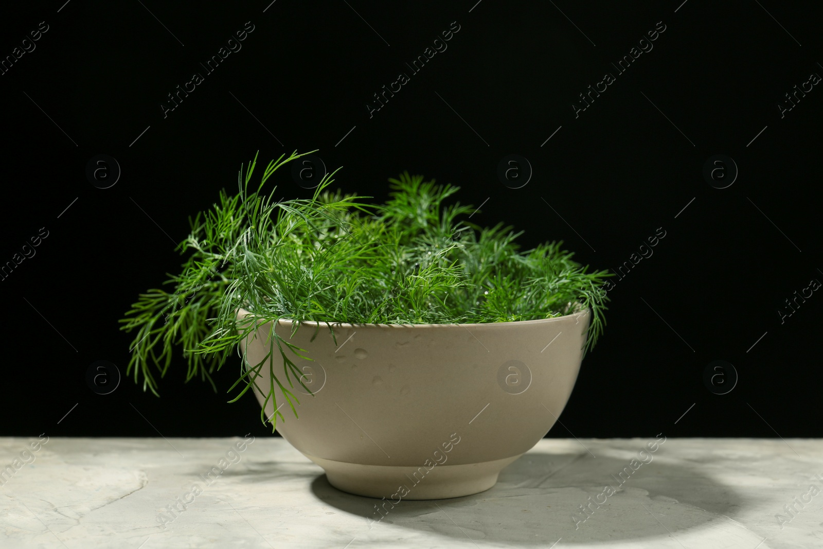 Photo of Bowl of fresh green dill with water drops on light grey table against black background