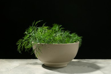 Photo of Bowl of fresh green dill with water drops on light grey table against black background