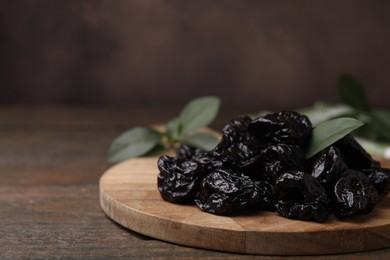 Photo of Tasty dried prunes and green leaf on wooden table, closeup. Space for text