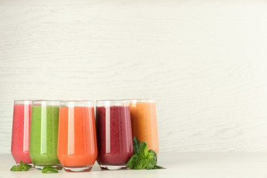 Colorful fruit smoothies and fresh mint on table against white wooden wall. Space for text