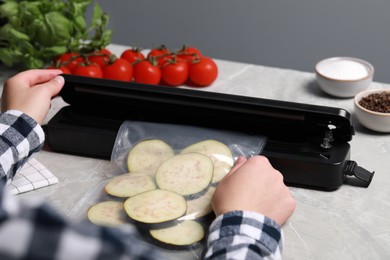 Photo of Woman packing cut eggplant into plastic bag using vacuum sealer on light grey marble table, closeup
