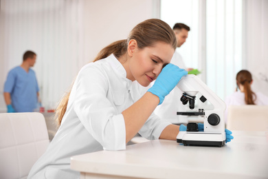 Scientist using microscope at table and colleagues in laboratory. Medical research