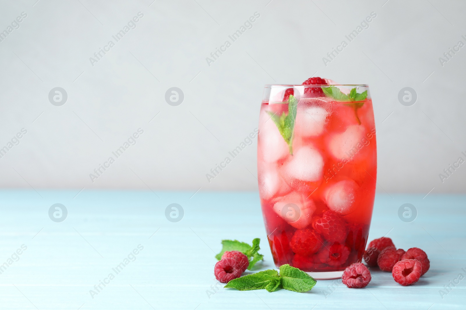 Photo of Glass of raspberry refreshing drink on blue wooden table, space for text