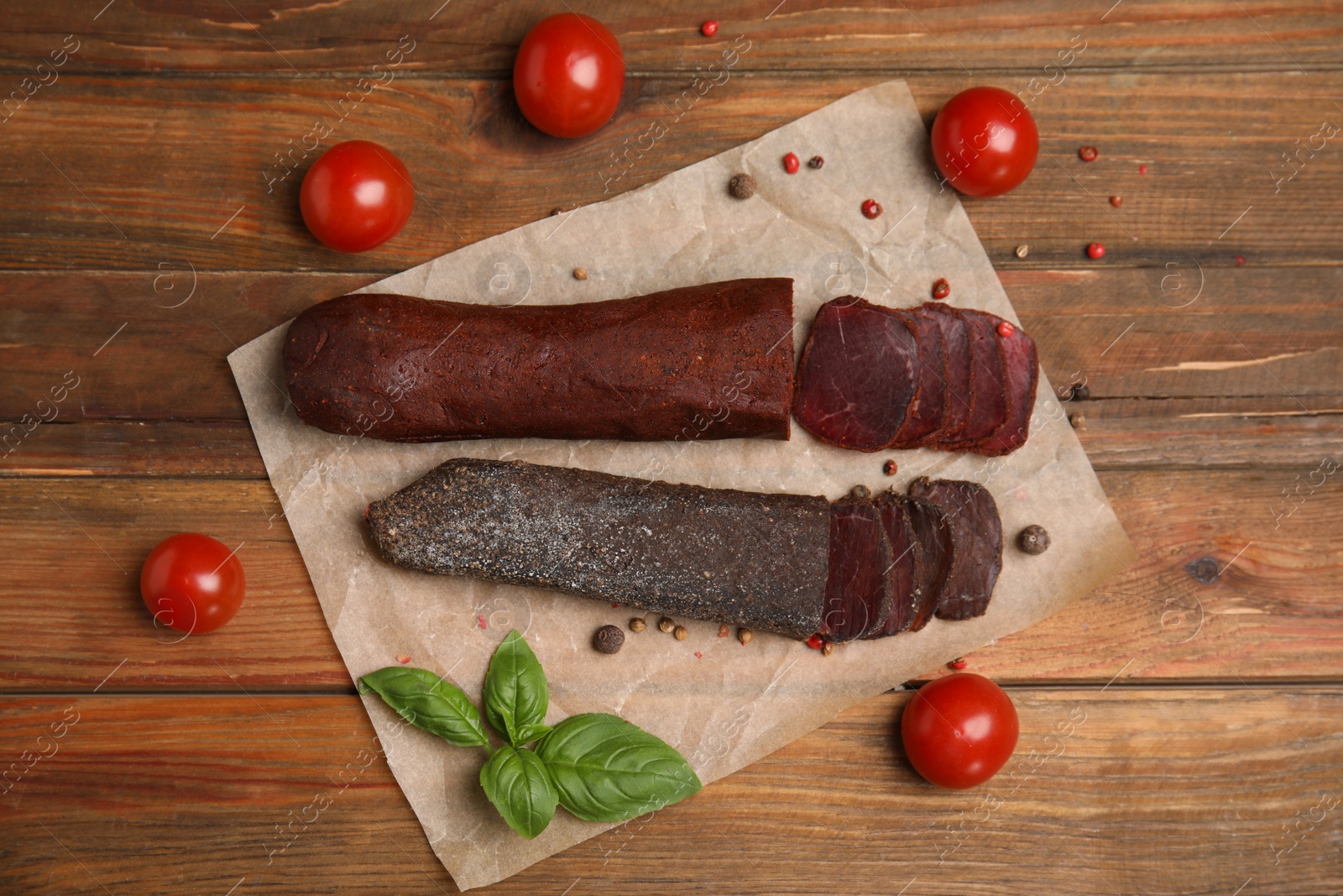 Photo of Delicious dry-cured beef basturma with basil and tomatoes on wooden table, flat lay