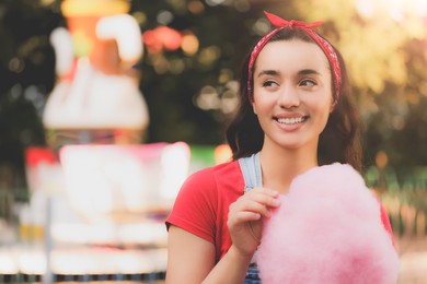 Stylish young woman with cotton candy at funfair on sunny day, space for text