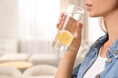 Photo of Young woman drinking lemon water at home, closeup. Space for text