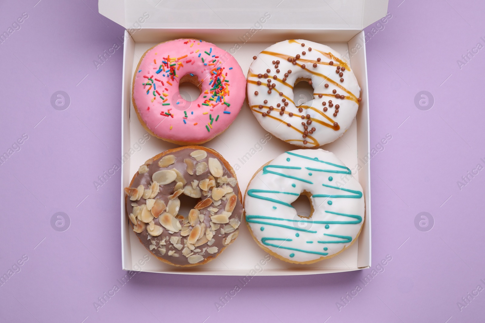 Photo of Box with different tasty glazed donuts on violet background, top view