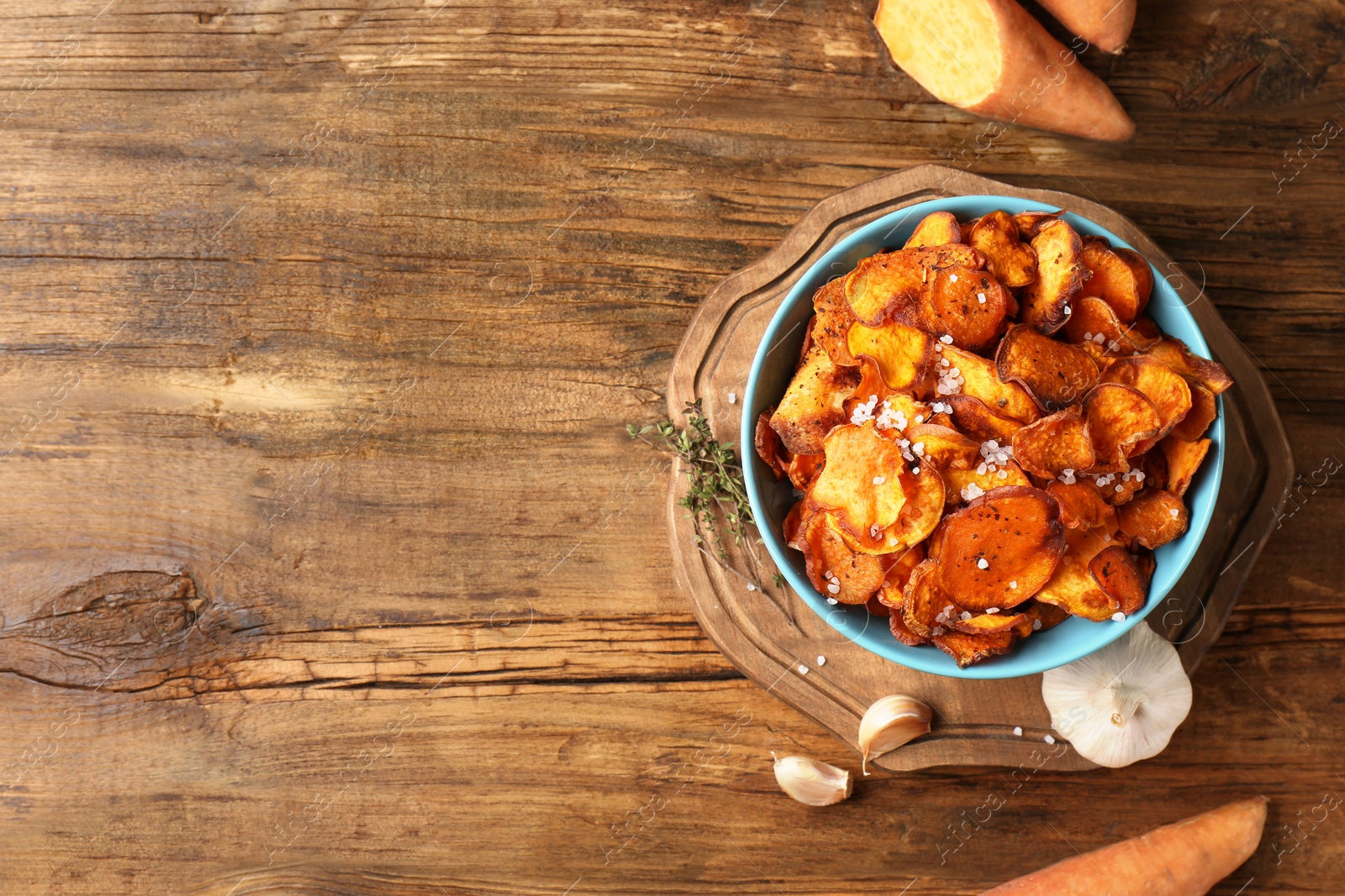 Photo of Flat lay composition with bowl of sweet potato chips on wooden table. Space for text