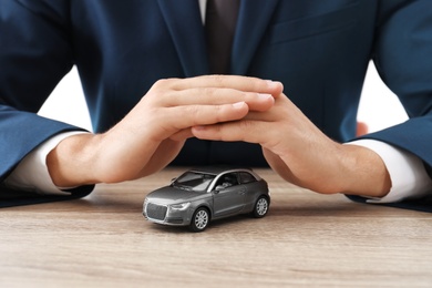 Insurance agent covering toy car on table, focus on hands