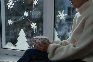 Photo of Woman with hot drink on sofa near beautifully decorated window at home, closeup