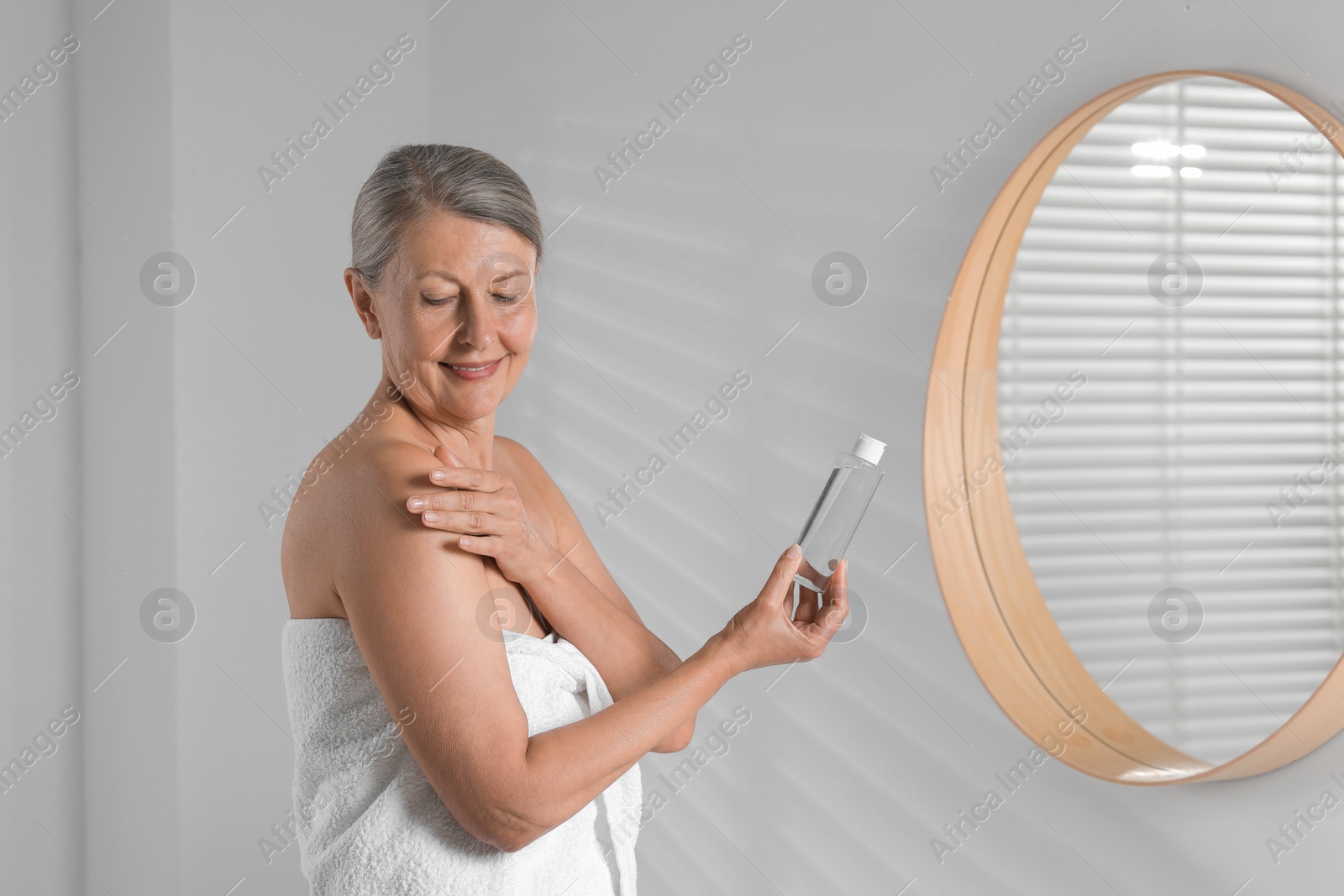 Photo of Happy woman applying body oil on shoulder in bathroom. Space for text