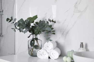 Photo of Towels, toiletries and glass vase with beautiful eucalyptus branches on bathroom counter. Interior design