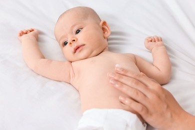 Woman applying body cream onto baby`s skin on bed, closeup